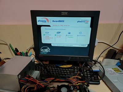 Picture of an IBM monitor showing the Phoenix AwardBIOS screen with the current connected devices and available RAM. A black keyboard is visible and wires around it from a power supply that connects to the motherboard which is barely in view